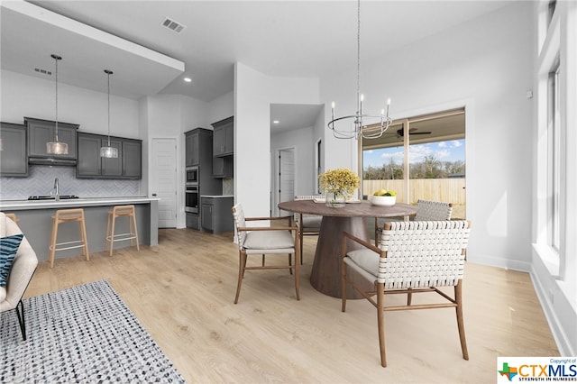 dining space with a high ceiling, light wood-type flooring, an inviting chandelier, and sink