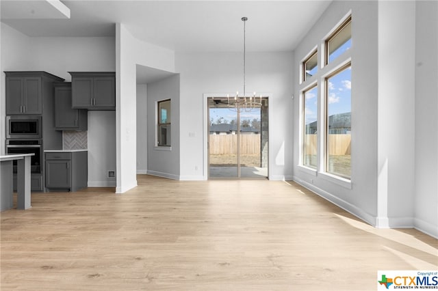 interior space with backsplash, a wealth of natural light, a chandelier, and stainless steel appliances