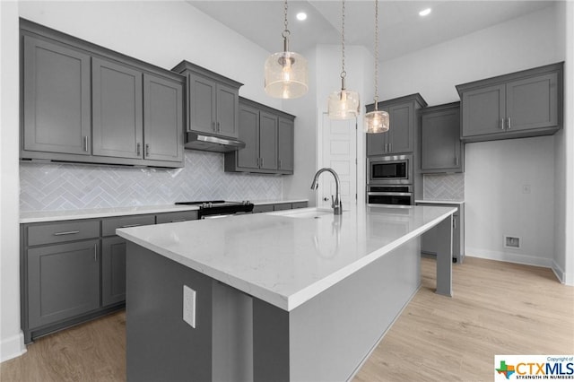 kitchen featuring sink, light wood-type flooring, an island with sink, decorative light fixtures, and stainless steel appliances