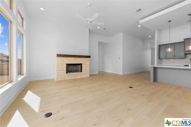 unfurnished living room featuring a high ceiling, light wood-type flooring, a stone fireplace, and ceiling fan