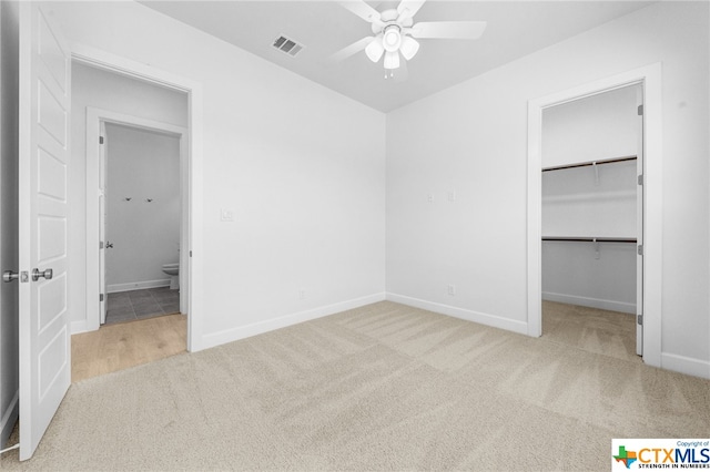 unfurnished bedroom featuring a walk in closet, ceiling fan, a closet, and light carpet