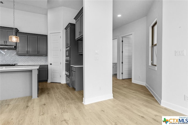 kitchen with decorative backsplash, gray cabinetry, stainless steel oven, pendant lighting, and light hardwood / wood-style floors