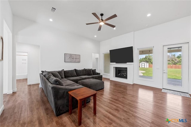 living room featuring wood finished floors, a glass covered fireplace, ceiling fan, visible vents, and recessed lighting