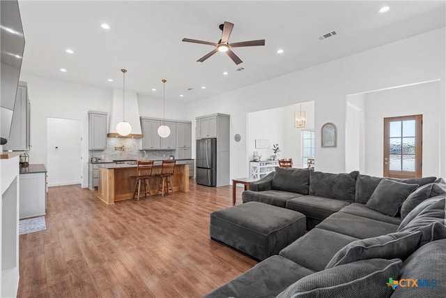 living room featuring a ceiling fan, visible vents, light wood finished floors, and recessed lighting