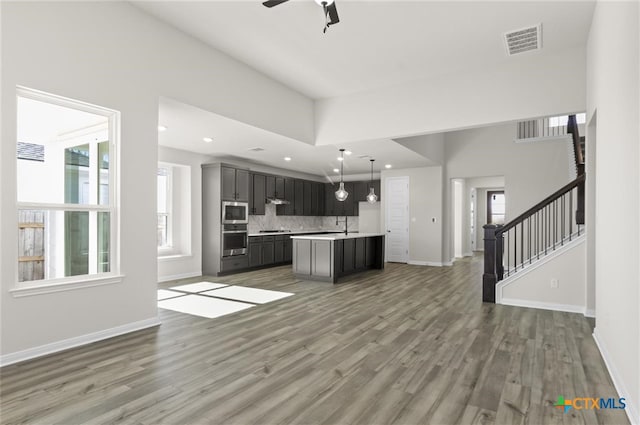 kitchen featuring appliances with stainless steel finishes, dark hardwood / wood-style flooring, tasteful backsplash, ceiling fan, and a center island with sink