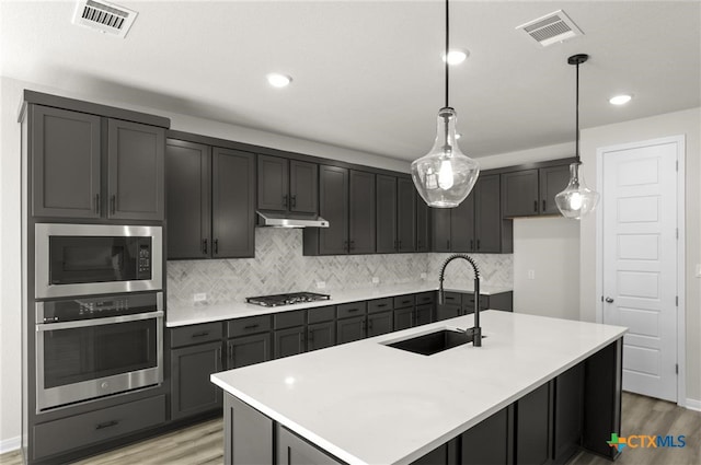 kitchen featuring hanging light fixtures, appliances with stainless steel finishes, a kitchen island with sink, and sink