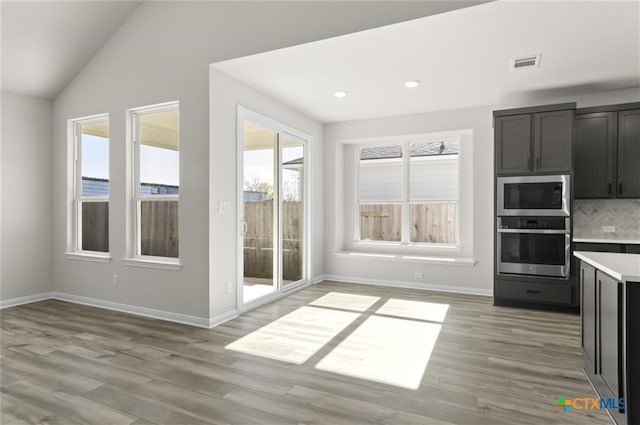 kitchen with light wood-type flooring, lofted ceiling, stainless steel appliances, and a wealth of natural light