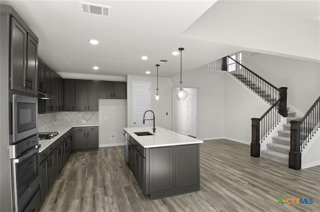 kitchen with decorative backsplash, stainless steel appliances, sink, hardwood / wood-style flooring, and a center island with sink