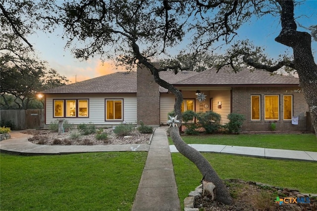 ranch-style home featuring a yard, fence, brick siding, and roof with shingles