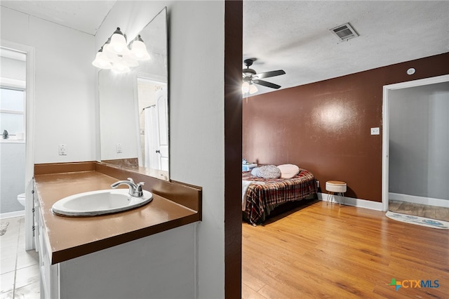 bathroom with ceiling fan, a textured ceiling, wood-type flooring, vanity, and toilet