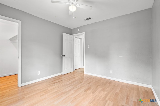 unfurnished bedroom with light hardwood / wood-style floors, ceiling fan, a closet, and a walk in closet