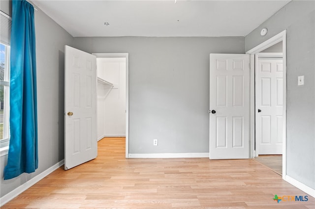 unfurnished bedroom with a closet, a walk in closet, and light hardwood / wood-style flooring