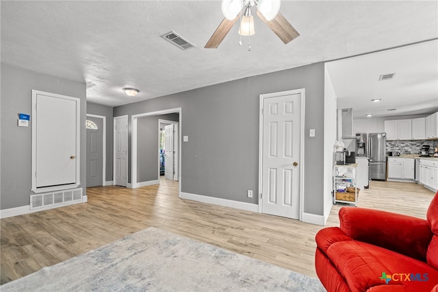 living room with ceiling fan, a textured ceiling, and light wood-type flooring