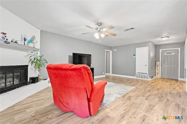 living room with a brick fireplace, light wood-type flooring, and ceiling fan