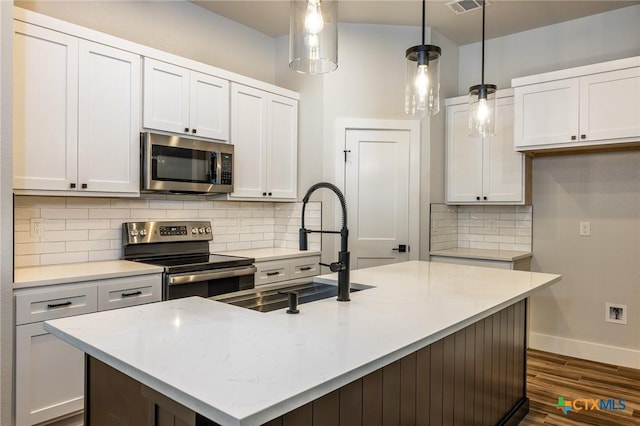 kitchen with a kitchen island with sink, decorative light fixtures, white cabinetry, and appliances with stainless steel finishes