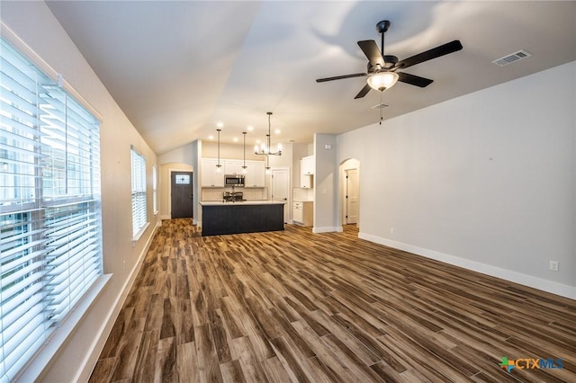 unfurnished living room with dark wood-type flooring, ceiling fan with notable chandelier, and vaulted ceiling