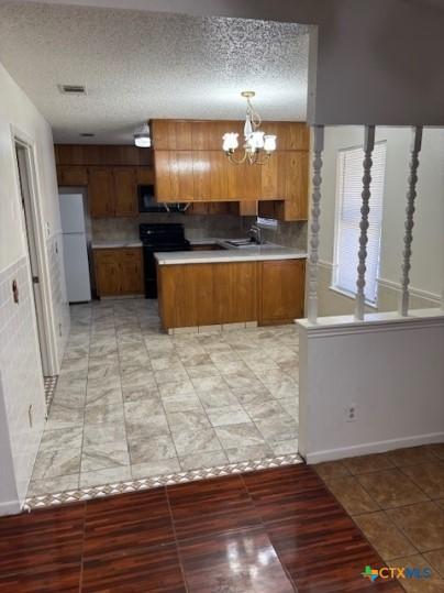 3206 Tallwood Dr, Killeen, TX 76549 - kitchen featuring freestanding refrigerator, brown cabinetry, a peninsula, a chandelier, and a textured ceiling