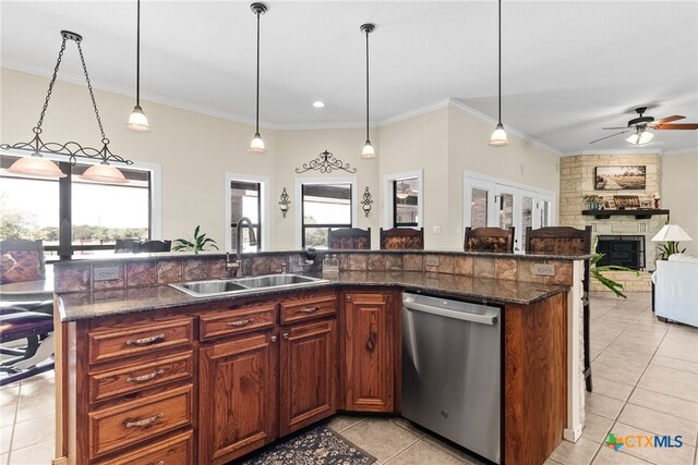 kitchen with a stone fireplace, hanging light fixtures, sink, a kitchen island with sink, and stainless steel dishwasher