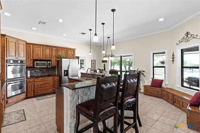 kitchen featuring appliances with stainless steel finishes, decorative light fixtures, sink, a breakfast bar, and a kitchen island with sink