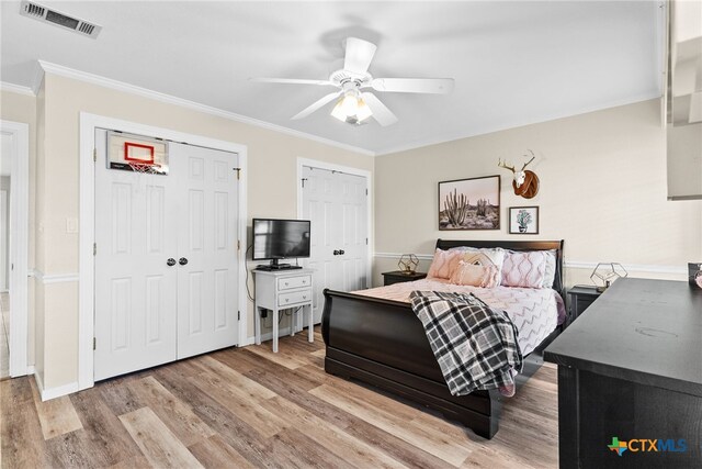 bedroom featuring two closets, hardwood / wood-style flooring, ceiling fan, and crown molding