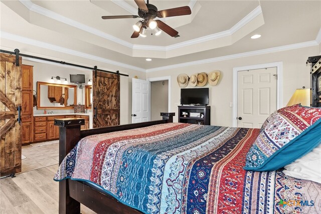 bedroom featuring ensuite bath, ornamental molding, ceiling fan, a tray ceiling, and a barn door