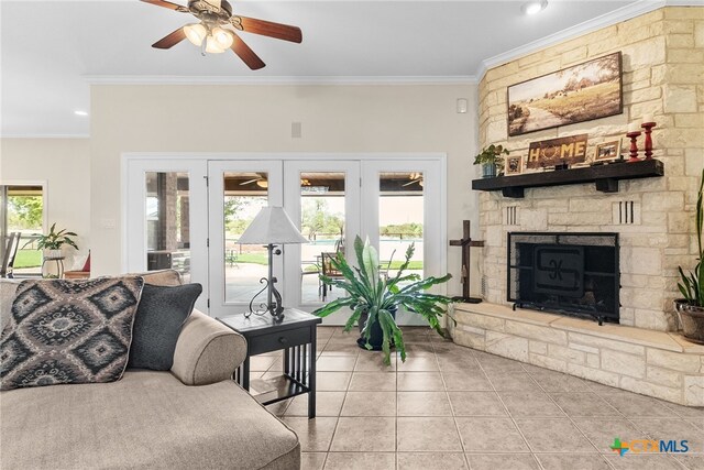 living room featuring a stone fireplace, light tile patterned floors, crown molding, and ceiling fan