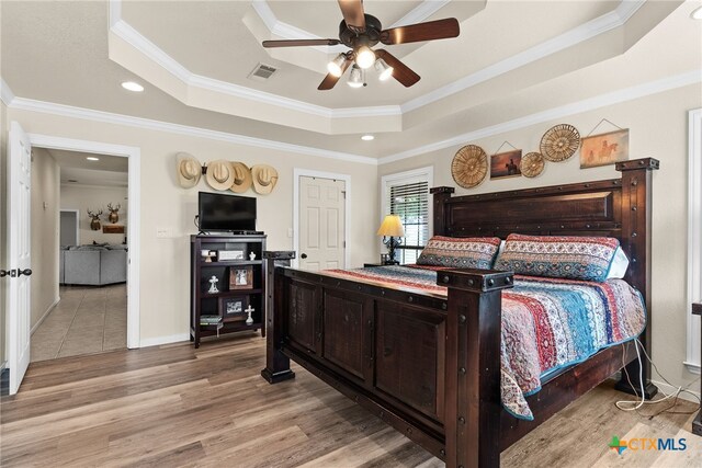 bedroom featuring light wood-type flooring, a tray ceiling, ceiling fan, and crown molding