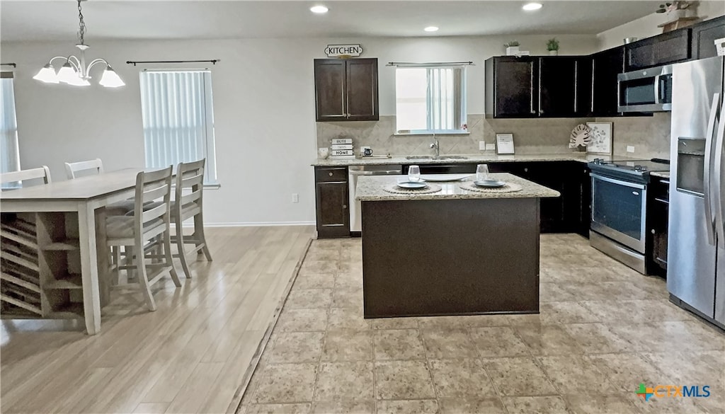 kitchen with appliances with stainless steel finishes, light stone countertops, hanging light fixtures, decorative backsplash, and a center island