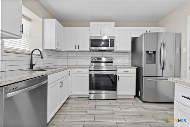 kitchen with sink, white cabinetry, backsplash, stainless steel appliances, and light stone counters