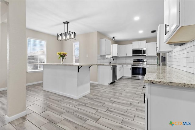 kitchen featuring white cabinetry, appliances with stainless steel finishes, pendant lighting, light stone countertops, and backsplash