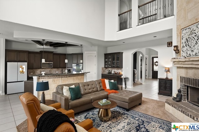 living room featuring a brick fireplace, a towering ceiling, and light tile patterned floors