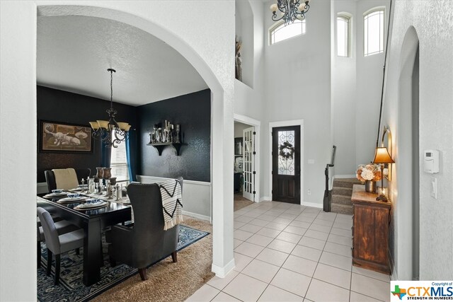 entrance foyer with a textured ceiling, light tile patterned floors, a high ceiling, and an inviting chandelier