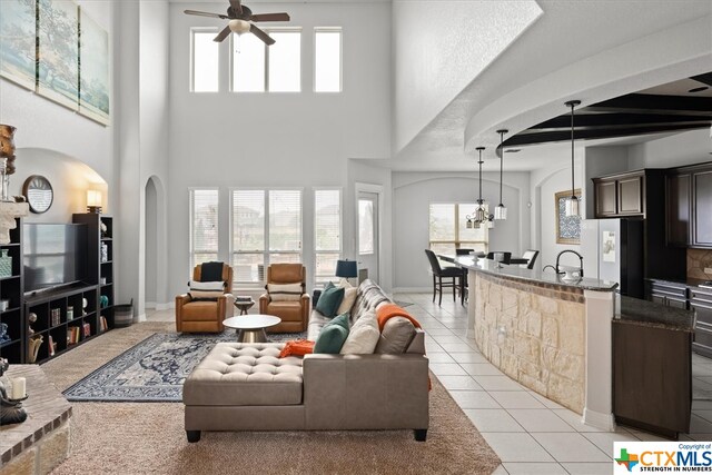 tiled living room with a towering ceiling, ceiling fan with notable chandelier, plenty of natural light, and beam ceiling