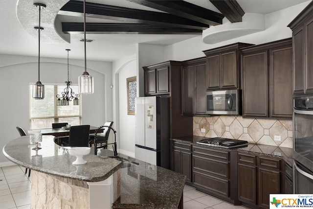 kitchen featuring stainless steel appliances, dark stone counters, a center island, a notable chandelier, and light tile patterned flooring