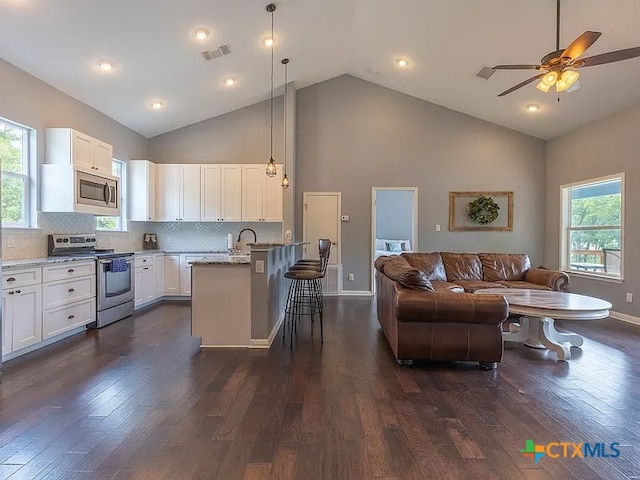 kitchen featuring light stone counters, stainless steel appliances, visible vents, open floor plan, and a kitchen breakfast bar