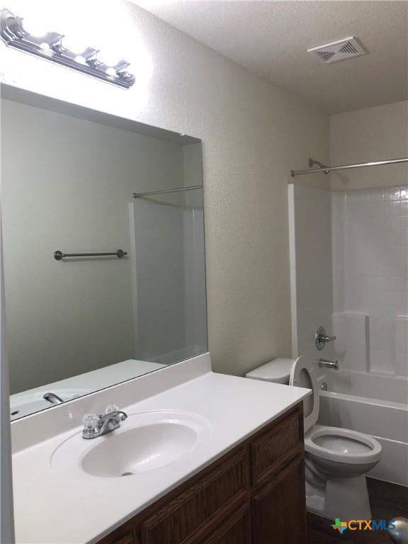 full bath featuring vanity, toilet, visible vents, a textured wall, and bathtub / shower combination
