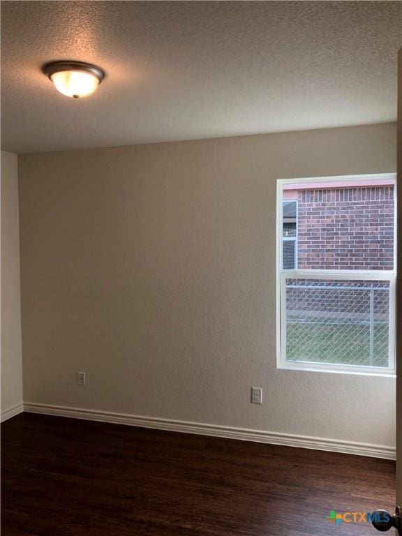 unfurnished room with a textured ceiling, dark wood finished floors, and baseboards