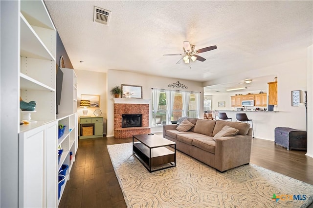 living room with a brick fireplace, visible vents, a textured ceiling, and hardwood / wood-style floors