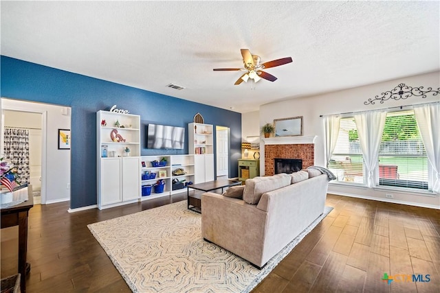 living room with a textured ceiling, a brick fireplace, dark wood finished floors, and visible vents