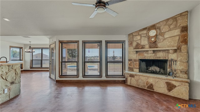 unfurnished living room featuring a stone fireplace and ceiling fan with notable chandelier