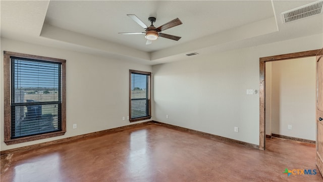 empty room featuring concrete flooring, ceiling fan, and a raised ceiling