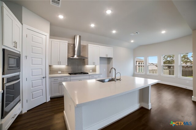 kitchen with stainless steel appliances, sink, wall chimney range hood, and an island with sink