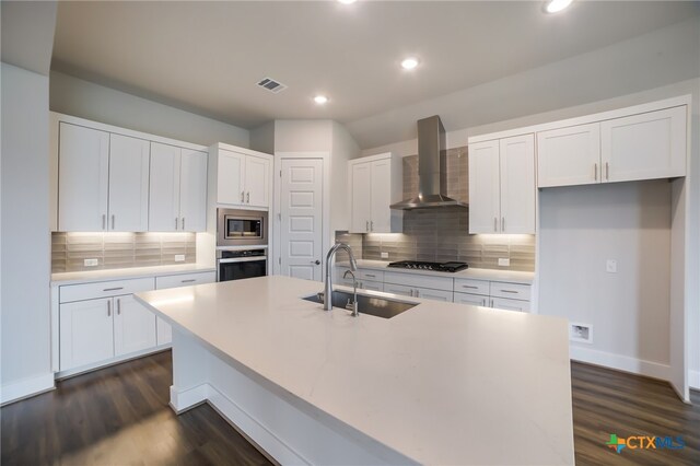 kitchen with stainless steel appliances, sink, white cabinets, wall chimney exhaust hood, and a kitchen island with sink