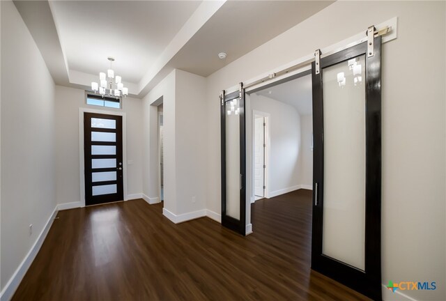 foyer entrance featuring a barn door, dark hardwood / wood-style floors, and an inviting chandelier