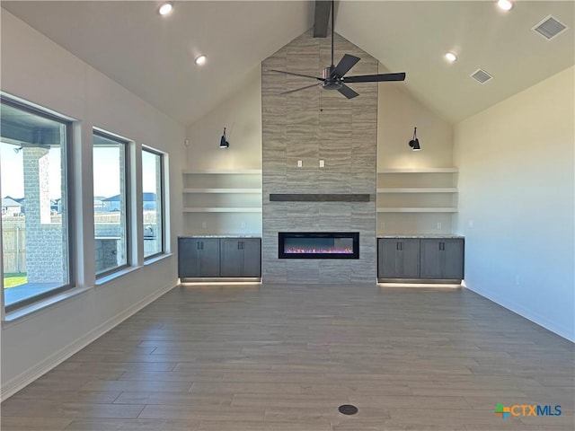 unfurnished living room with a tile fireplace, beamed ceiling, ceiling fan, high vaulted ceiling, and hardwood / wood-style flooring