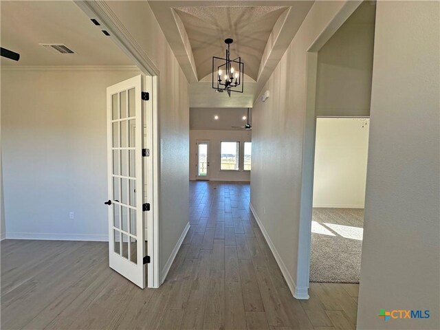 corridor featuring french doors, a raised ceiling, hardwood / wood-style floors, a chandelier, and crown molding