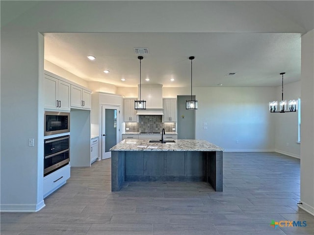 kitchen with oven, white cabinets, tasteful backsplash, light stone countertops, and a center island with sink