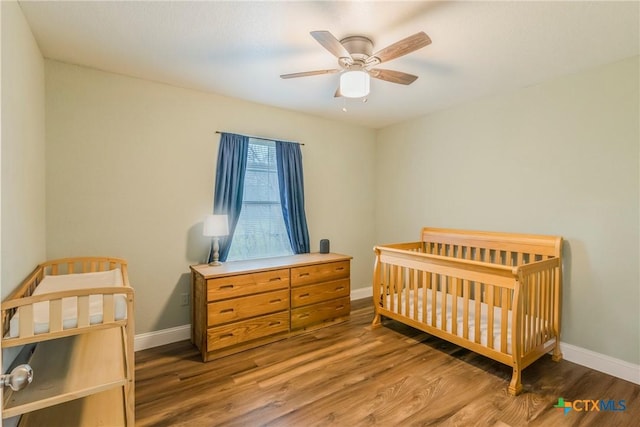 bedroom with ceiling fan, dark wood-type flooring, and a nursery area