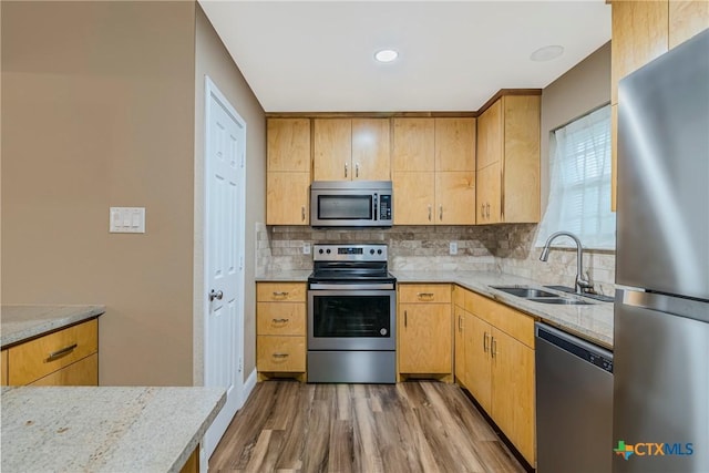 kitchen with appliances with stainless steel finishes, decorative backsplash, sink, and light stone countertops