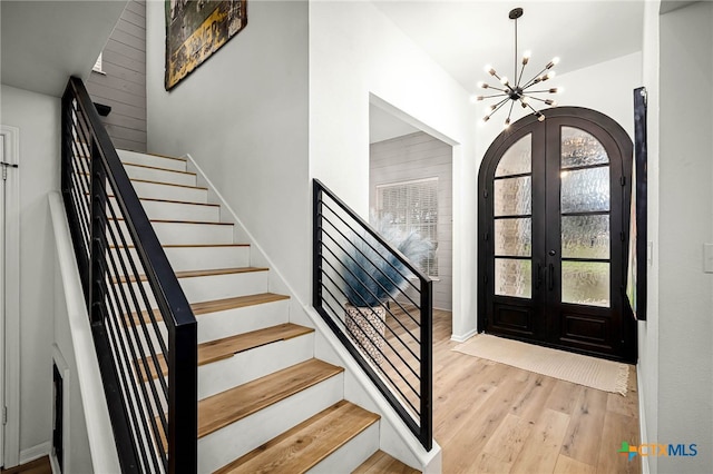 entrance foyer with wood finished floors, french doors, arched walkways, a chandelier, and stairs